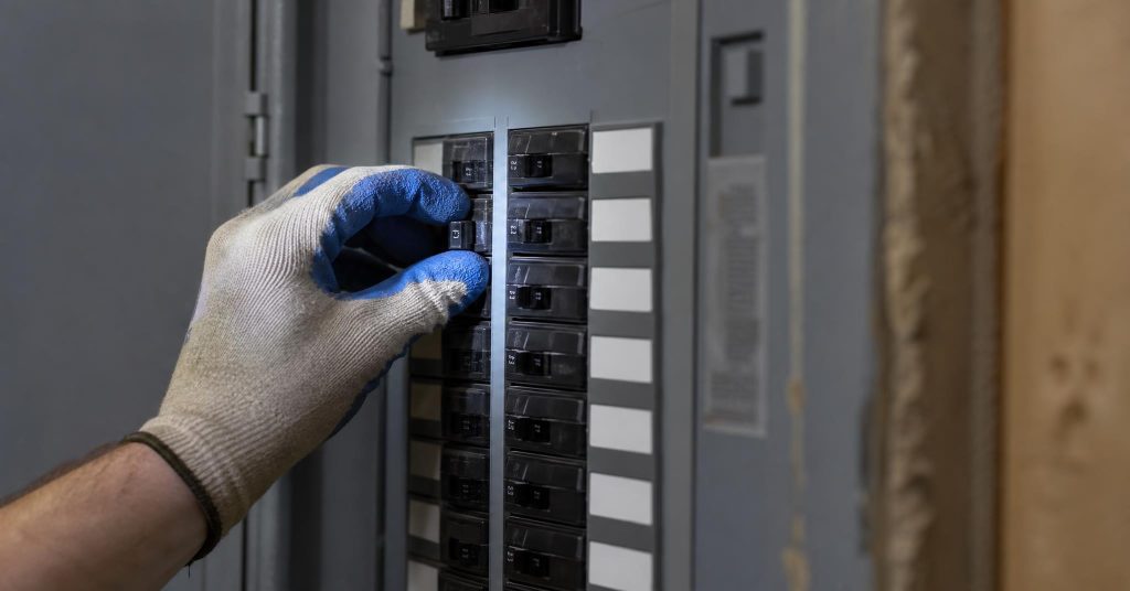 Gloved hand resetting a single circuit breaker inside a labeled residential panel.
