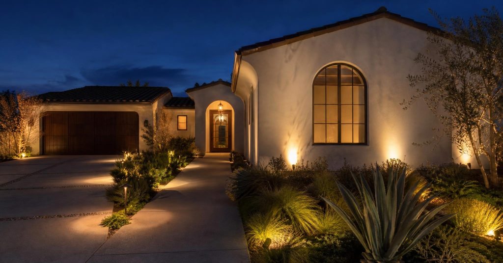 Warm outdoor path lights and uplighting on the stucco facade of a home at twilight.